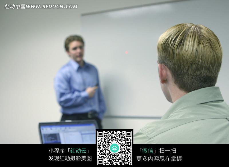 电脑前的<em>黄头发男人</em>跟远处的蓝衬衫<em>男士</em>谈话图